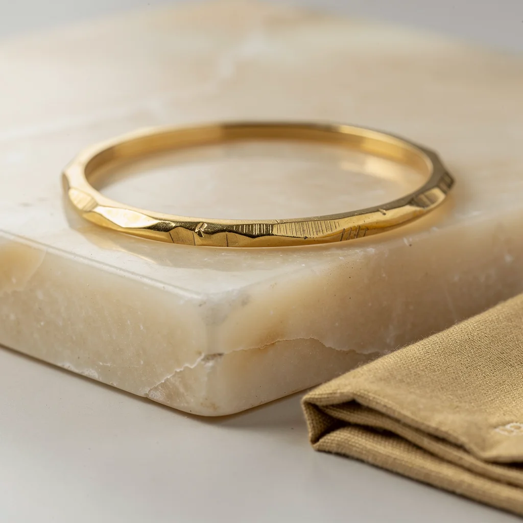 Brazalete rígido bañado en oro con superficie orgánica sobre fondo de taller
